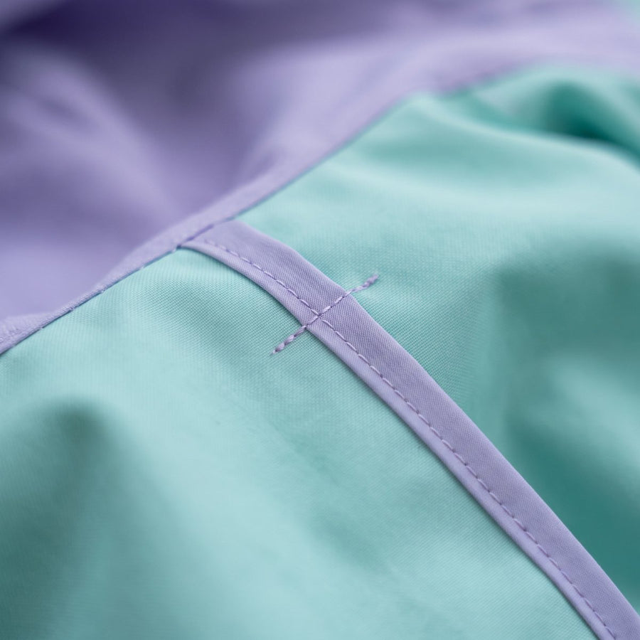 Close-up of the inside of a poncho: a seam neatly bound in lilac tape on seafoam fabric