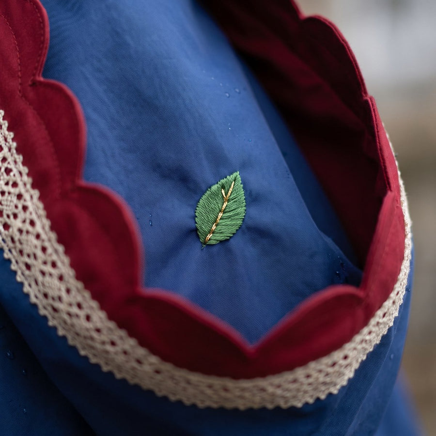Close-up of the FAIREST hem turned back to show a tiny embroidered green leaf with a gold vein