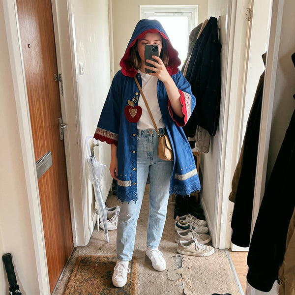 Mirror selfie in a hallway: FAIREST poncho worn over a white tee, jeans and sneakers